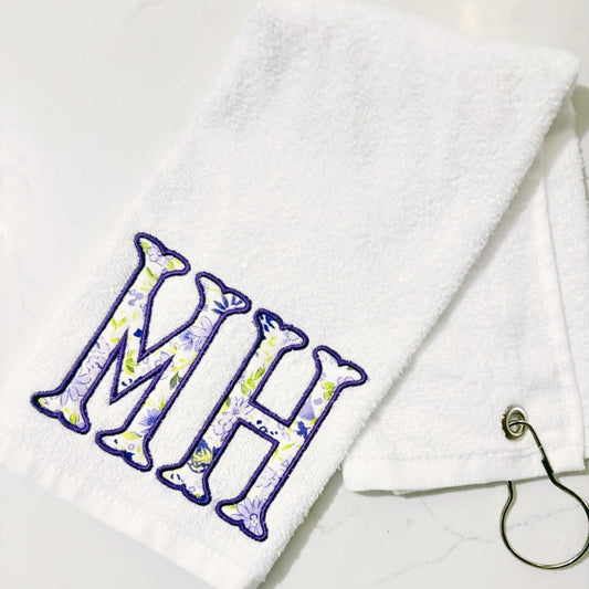 White towel with floral initials 'MH' on a white background