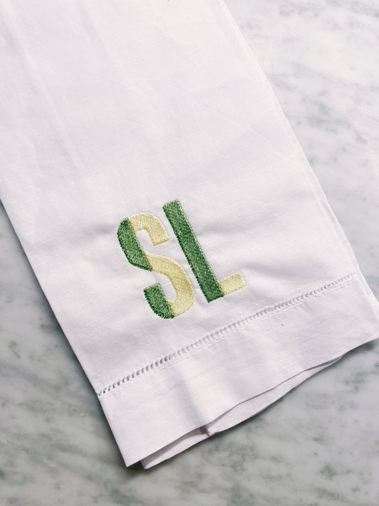 White towel with green and yellow embroidered initials on a marble surface