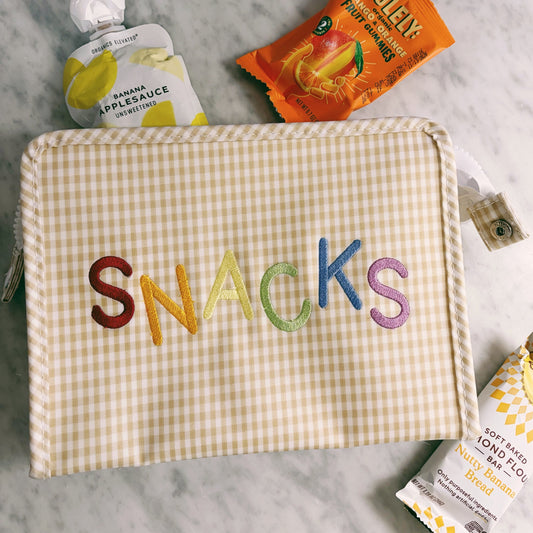 Checkered pouch with 'SNACKS' in colorful letters on a marble surface with snacks around.