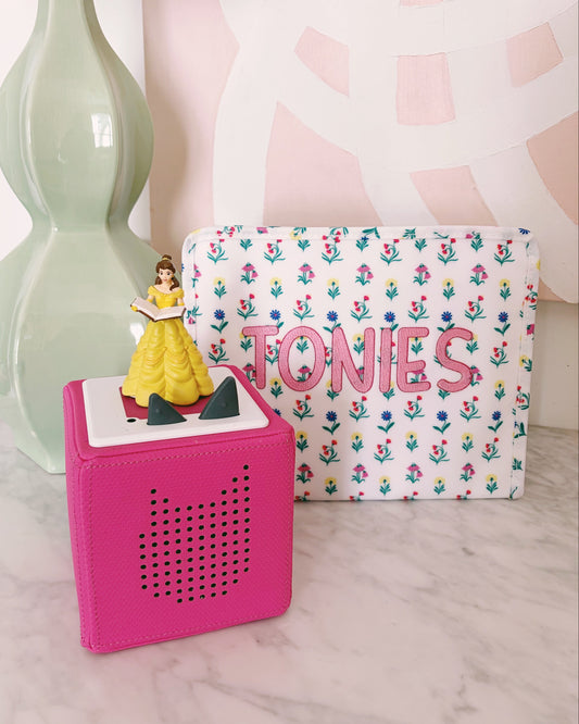 Small figurine of a princess on a pink block with a floral-patterned pouch labeled 'TONIES' in the background.