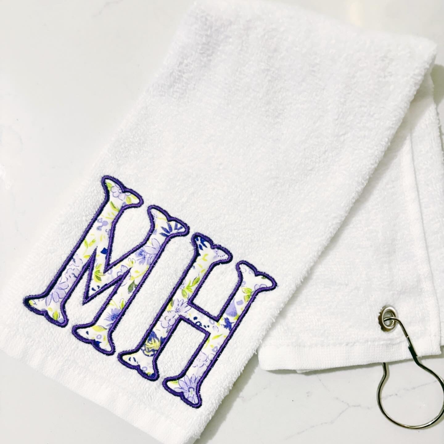 White towel with floral initials 'MH' on a white background