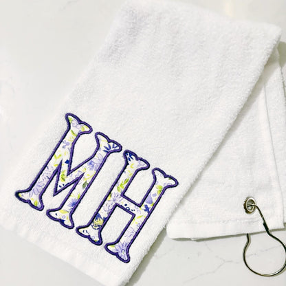 White towel with floral initials 'MH' on a white background