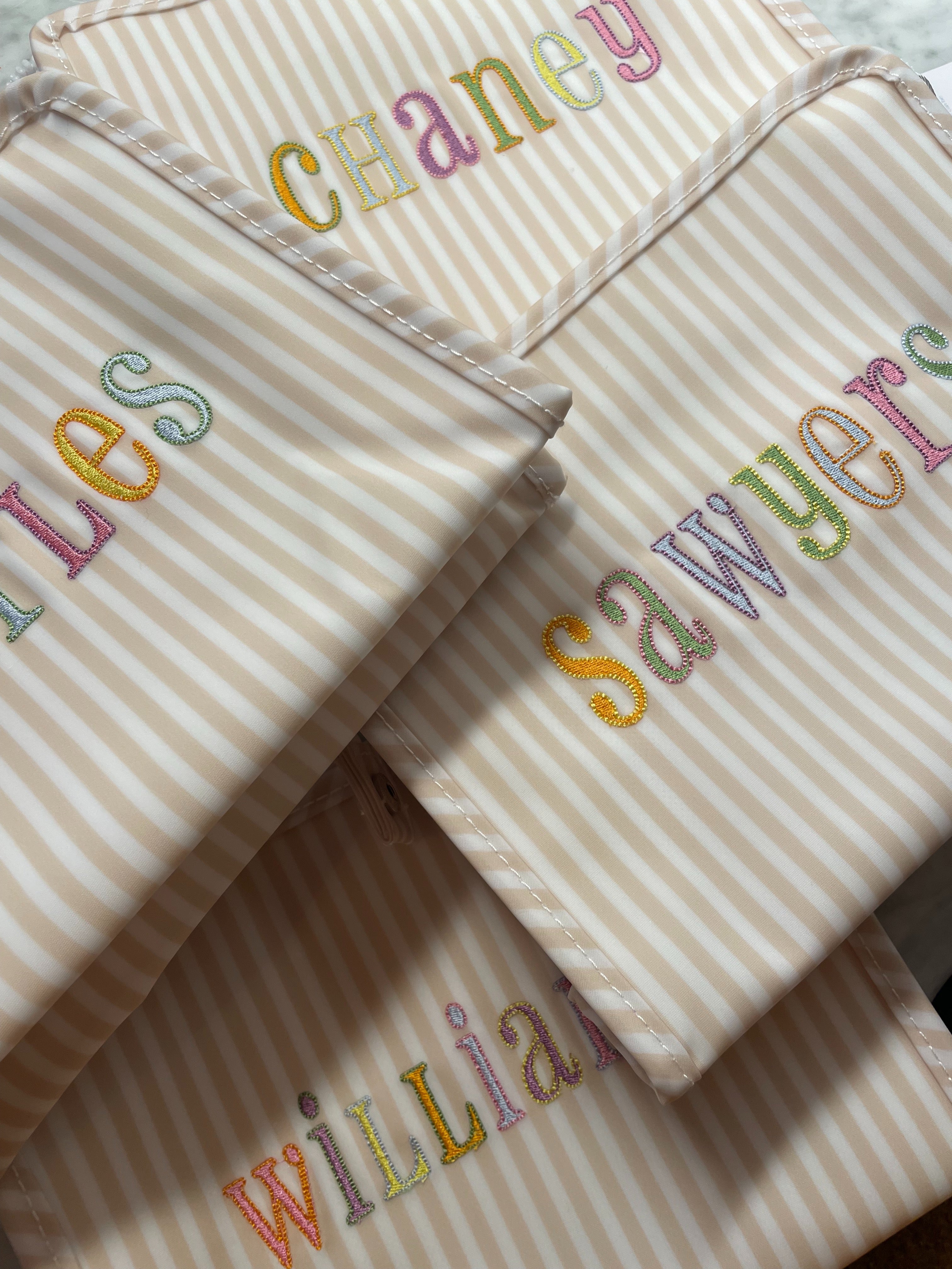 Folded striped fabric with embroidered names in various colors on a neutral background