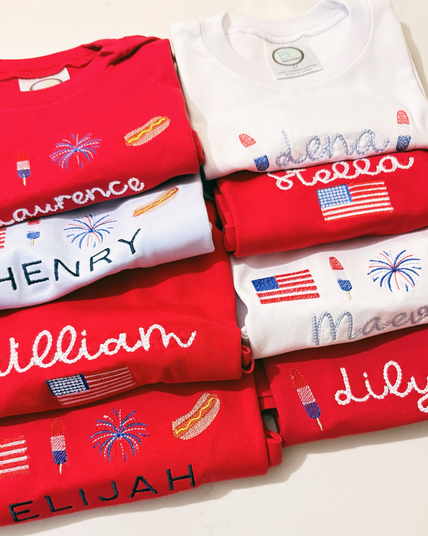 Stack of red and white t-shirts with embroidered names and designs.