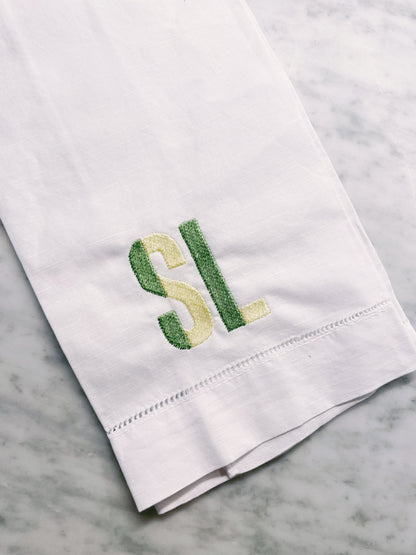 White towel with green and yellow embroidered initials on a marble surface