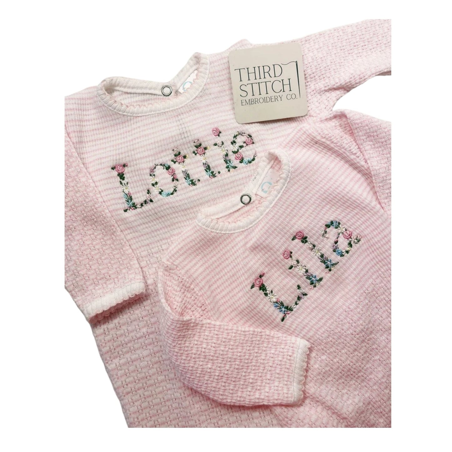 Pink baby outfit with floral embroidery on a white background