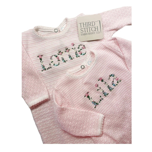 Pink baby outfit with floral embroidery on a white background