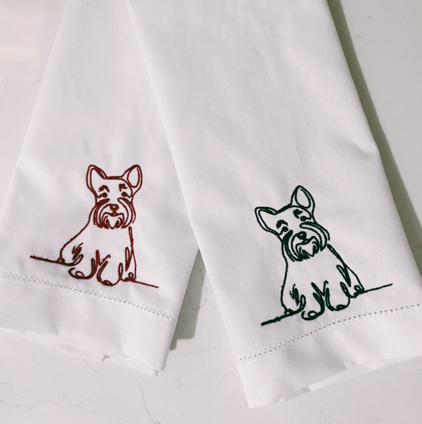 Two white napkins with embroidered dog designs on a light background
