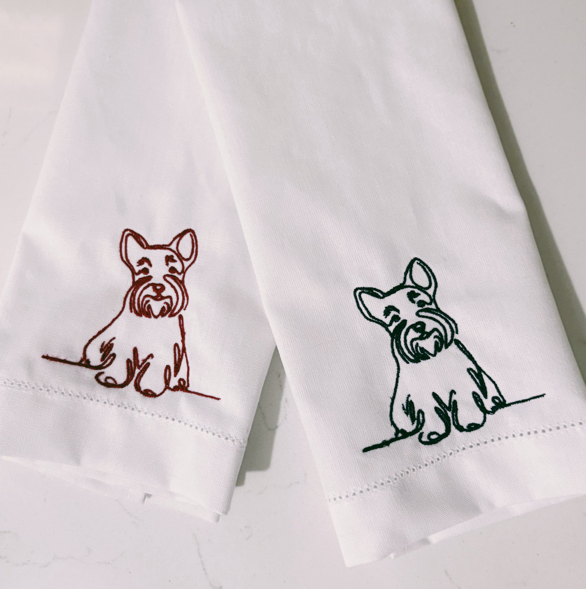 Two white napkins with embroidered dog designs on a light background
