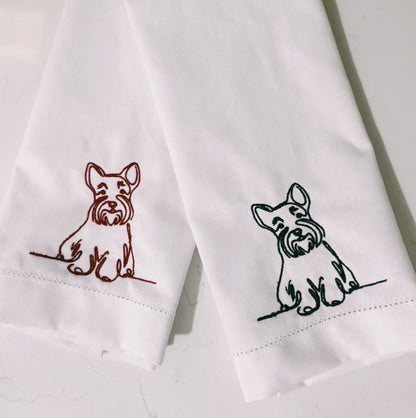 Two white napkins with embroidered dog designs on a light background