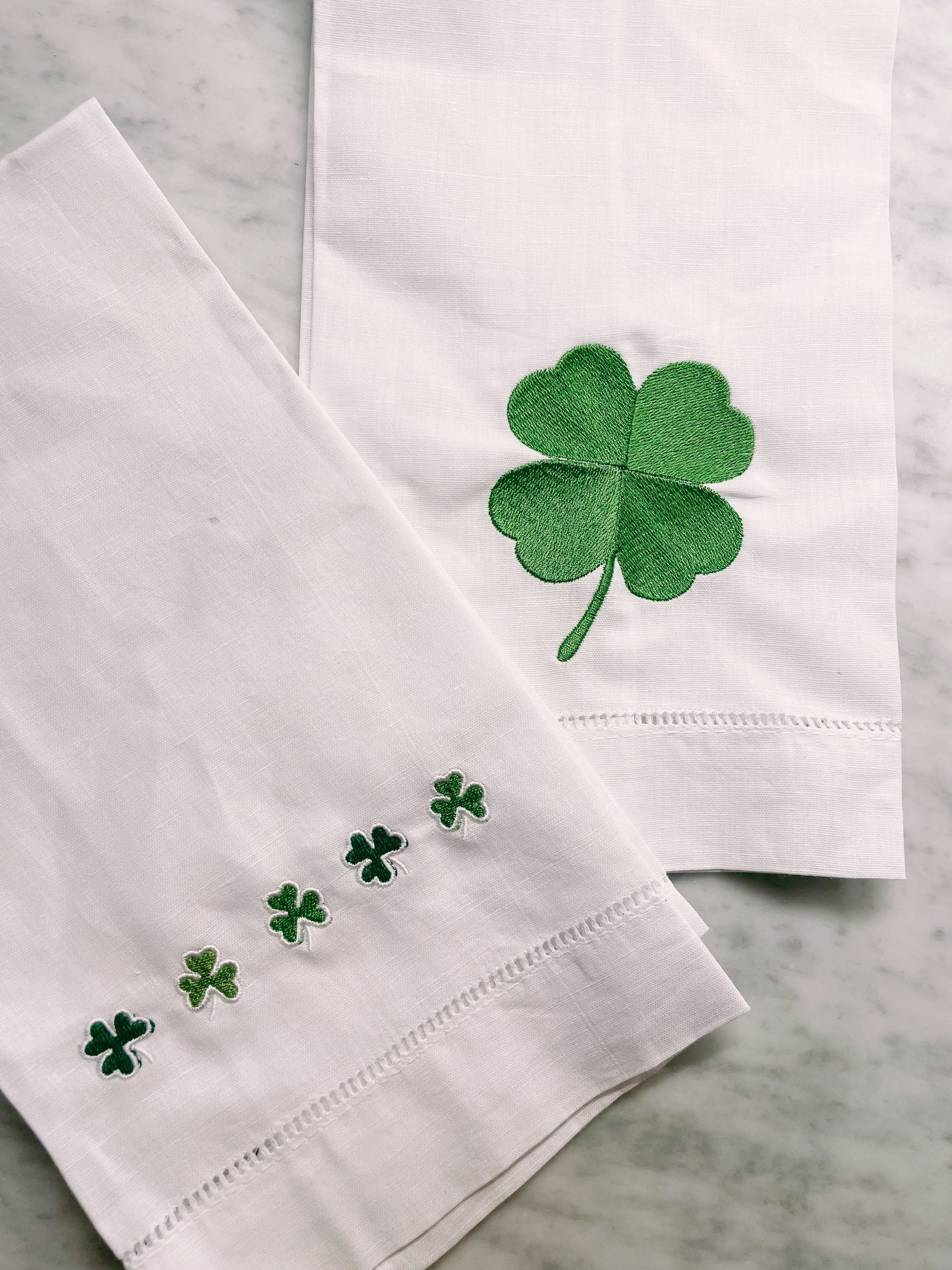 White napkins with green four-leaf clover designs on a marble surface