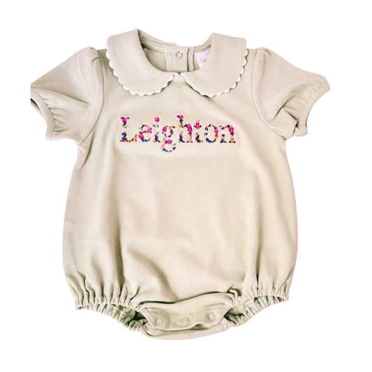 Beige baby romper with colorful embroidered name on a white background