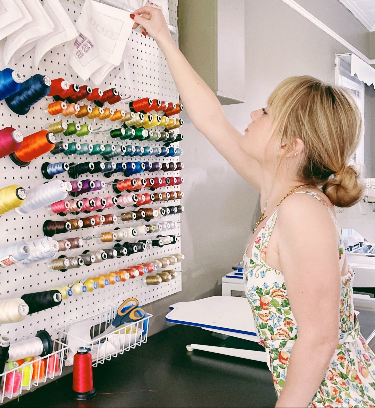 Woman selecting thread from a pegboard with colorful spools in a sewing room.