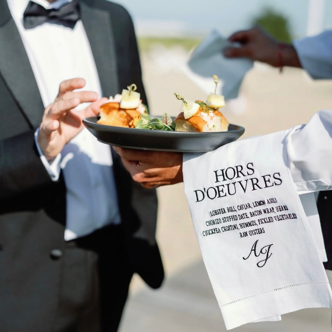 Person in formal attire holding a plate of hors d'oeuvres with a menu card in the foreground.